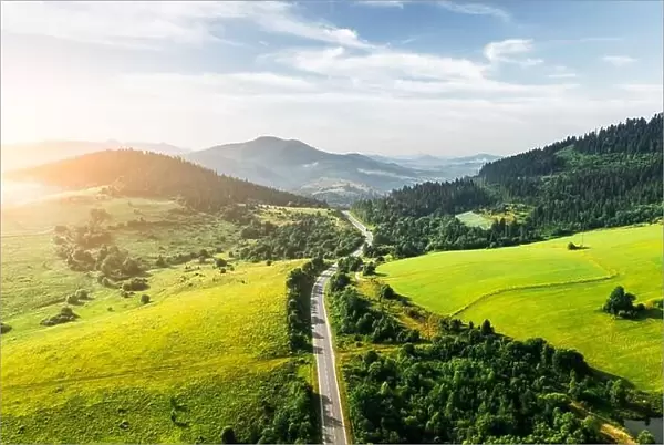 Flight over the summer mountains with mountain road serpentine, green fields and forest. Ukraine, Carpathian mountains. Landscape photography