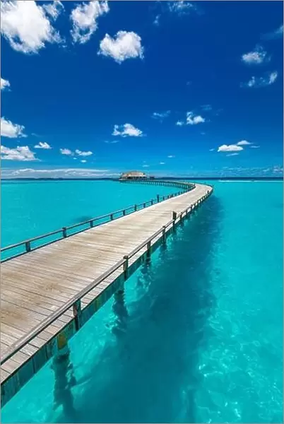 Maldives villa on piles on water, luxury summer travel. Morning sunlight, long wooden jetty under cloudy blue sky. Luxury bungalows, amazing sea