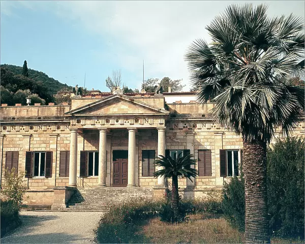 Main facade of Napoleon's Villa of San Marino in Portoferraio, on the island of Elba. The entrance is characterized by a porch with a gable on four columns. In the foreground a palm tree in the garden in front