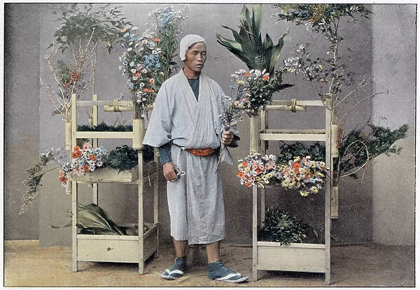 A Japanese flower seller stands by a portable stall made of bamboo with integral holders