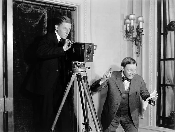 Two men making a film using a movie camera indoors in Americ
