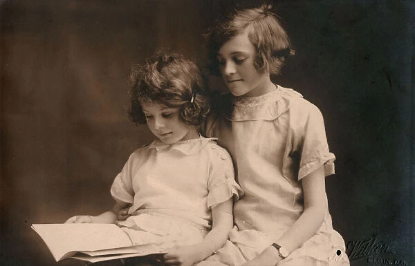 Older girl helps her younger sister read a book