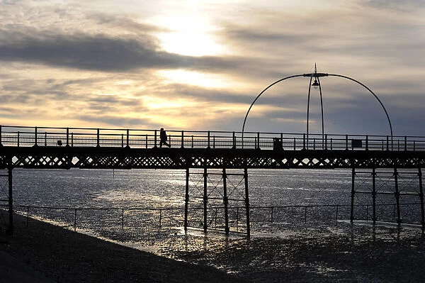 Silhouette of boy running along Southport Pier at sunset