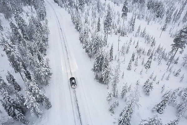 Aerial shot of a car crossing the boreal forest covered with snow, Akaslompolo, Finnish Lapalnd, Finland, Scandinavia, Europe