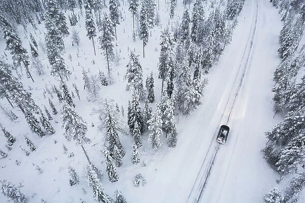 Aerial view of a car driving through the snow covered forest on icy road, Akaslompolo, Finnish Lapland, Finland, Scandinavia, Europe
