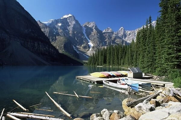 Canoes for hire on shore of Moraine Lake, with view to the Wenkchemna Peaks