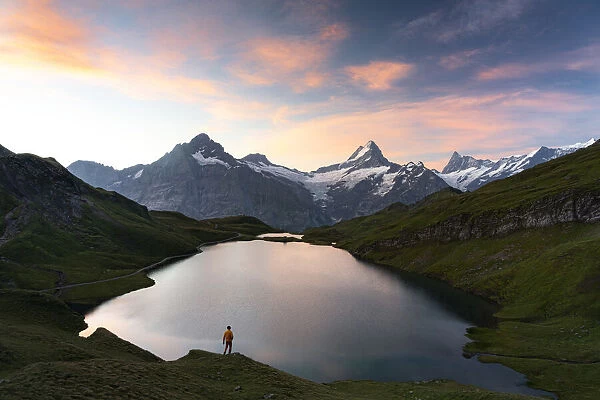 Hiker admiring sunrise from the shores of Bachalpsee lake, Grindelwald, Bernese Oberland