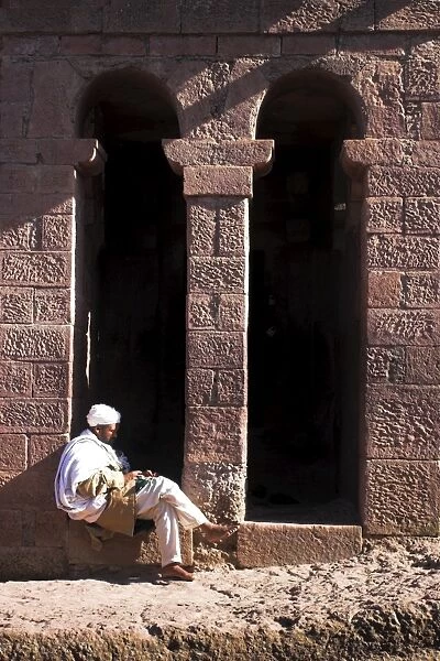 Pilgrim sits in early morning sun reading his Holy Bible at entrance doors to Bet Maryam church