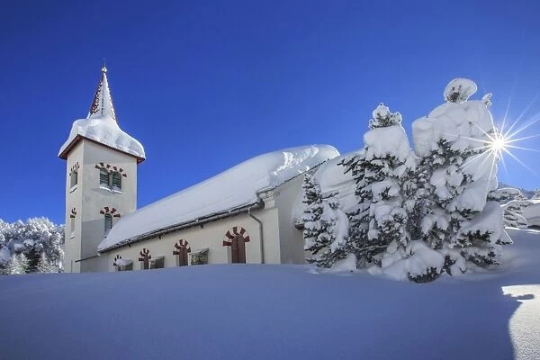 Rays of winter sun illuminate the snowy landscape and the typical church, Maloja