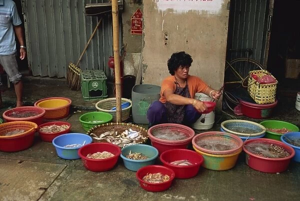 Woman squatting on the pavement selling fish from plastic bowls in the fish market at Taio on Lantau Island, Hong Kong