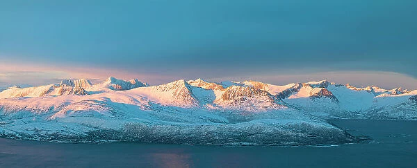 Aerial panoramic view of Senja mountain peaks covered with snow at dawn from Sommaroy, Troms county, Norway