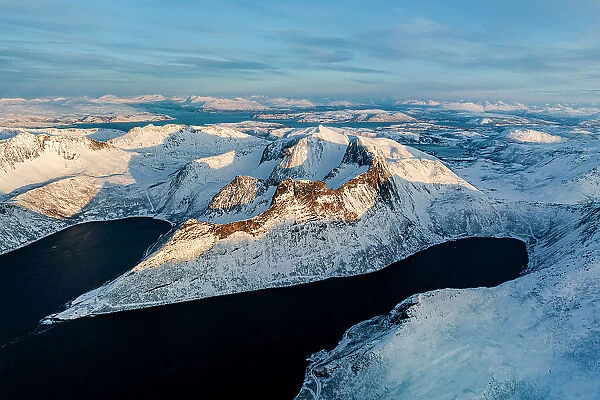 Aerial view of Oksfjord village and Grytetippen mountain covered with snow overlooking the cold sea, Senja, Troms county, Norway