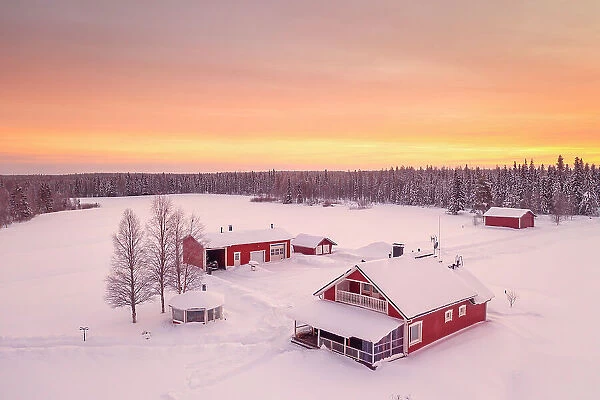 Europe, Finland, aerial view of a group of red buidlings on a frozen lake with the sun rising near Rovaniemi