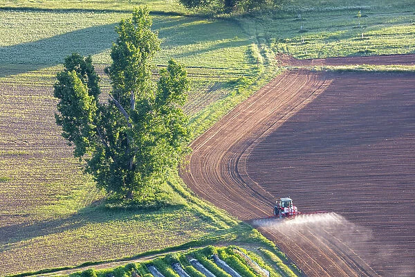 France, Nouvelle-Aquitaine, Dordogne, Perigord, Domme, a tractor sprays a field near Domme