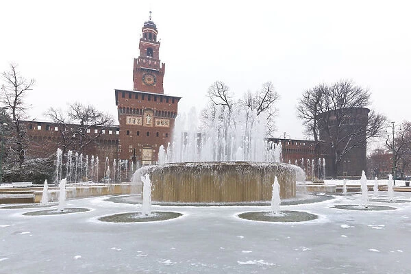 A iced fountain and Sforzesco Castle after a snowfall. Milan, Lombardy, Northern Italy