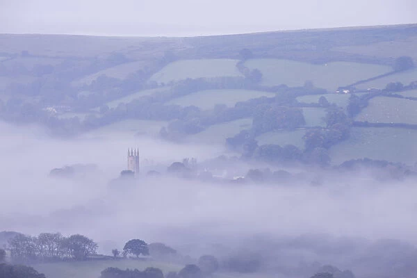 Morning mist swirls around the church tower of Widecombe in the Moor, Dartmoor, Devon