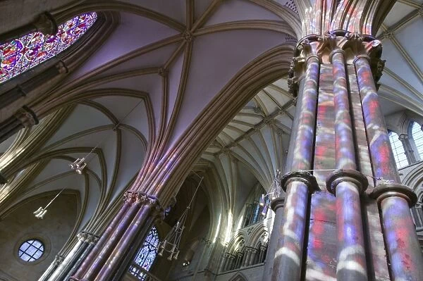 Light from stained glass windows on pillars in Lincoln Cathedral UK