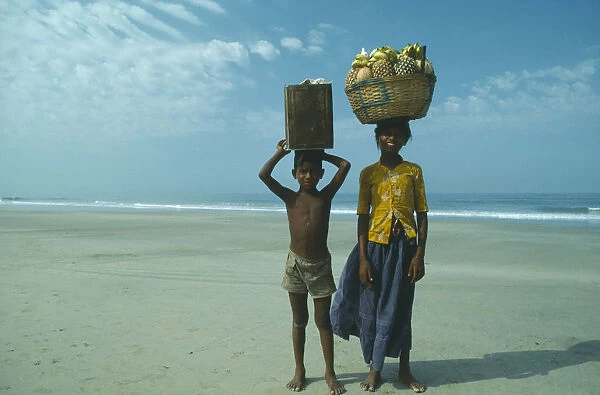 10015526. INDIA Goa Colva Boy and girl from Karnataka on beach carrying fruit