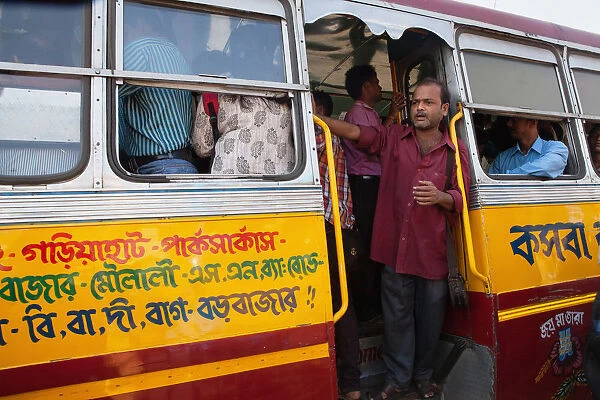 India, West Bengal, Kolkata, A bus conductor stands in the foot well of a public bus