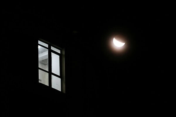 The light shines in the window of a building during a partial lunar eclipse in