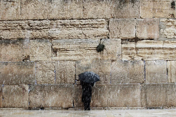 A man holding an umbrella prays at the Western Wall in Jerusalems Old City during a