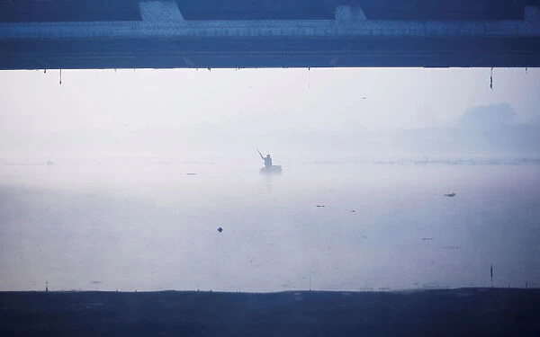 A man paddles a handmade boat across the Yamuna river on a foggy winter morning in New