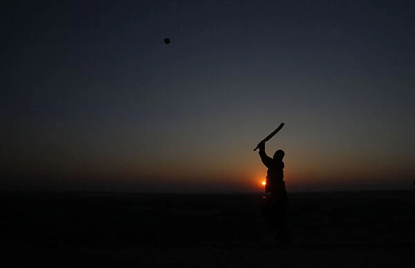 A man is silhouetted against the setting sun as he plays cricket at a park in Lahore