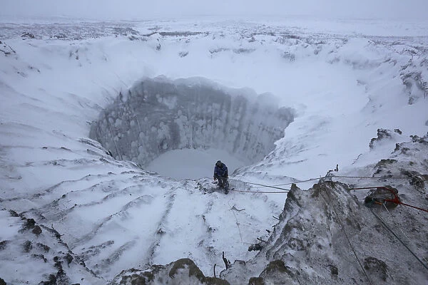A member of an expedition group stands on the edge of a newly formed crater on the Yamal Peninsula