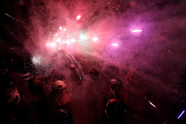Participators wearing motorcycle helmets get sprayed with firecrackers