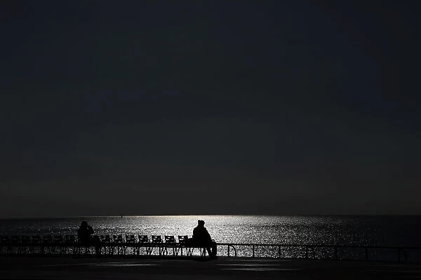 Sunlight reflects on the waters surface as people sit on chairs on a warm