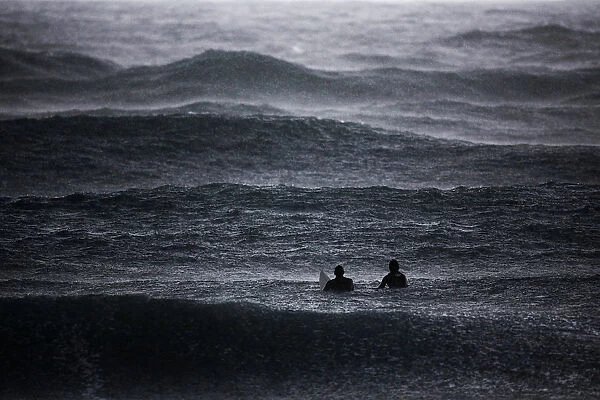Surfers wait to catch a wave in the Mediterranean Sea as it rains in Israels southern