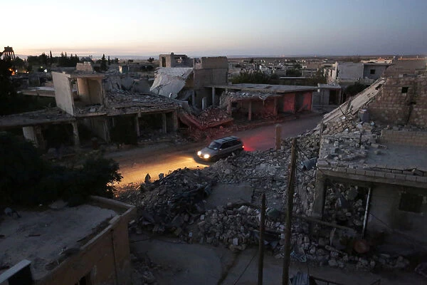 A vehicle drives past damaged buildings in the northern Syrian rebel-controlled town of