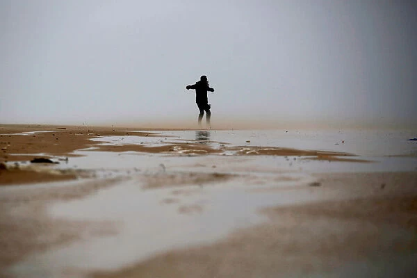 A woman walks against the wind during a storm in Zikim beach