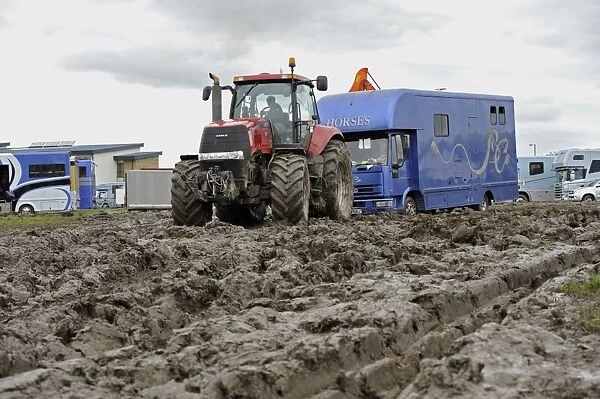Case tractor pulling horse lorry out of muddy carpark at agricultural show, which was cancelled due to bad weather