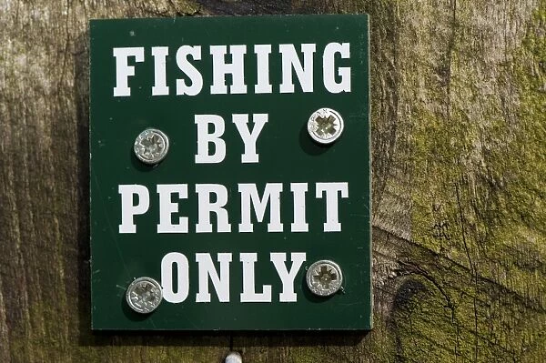 Fishing By Permit Only sign on post beside lake, England, april