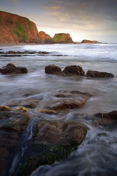 View of rocks on beach in cove at sunset, Westcombe Beach, Devon, England