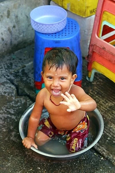 Young boy bathing in a bowl in the street, Yangon, Myanmar