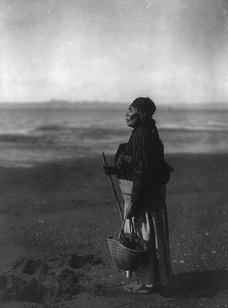 American Indian woman standing holding basket on beach, c1910. Photograph by Edward Curtis