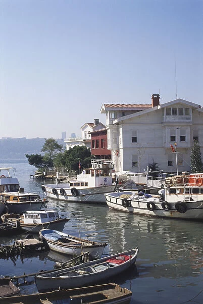 Asia, Turkey, Goksu River, various boats moored on the riverfront, cluster of buildings on waterfront, trees on edge, water and hilltop in background