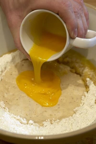 Beaten egg being poured into mixture of yeasty milk, flour, sugar and spices to make stollen