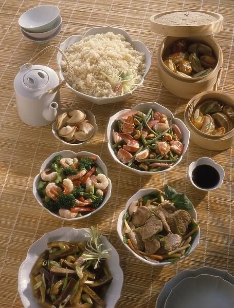 Bowls of Chinese food laid out on bamboo mat, including Dim sum, Szechuan lobster, stir-fried prawns and broccoli, pork stir-fry, Szechuan aubergine, rice, fortune cookies and tea pot