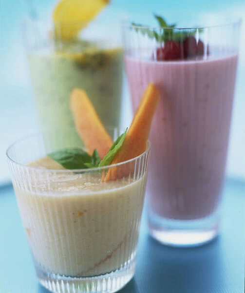 Colourful fruit smoothies in glasses decorated with basil leaves and pieces of fruit