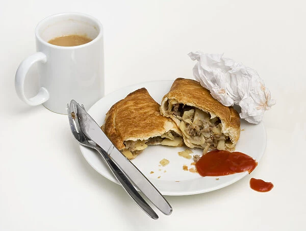 Cornish pasty, stuffed with beef, potatoes and onions, served on a plate with tomato ketchup, cutlery, crumpled napkin, mug of tea