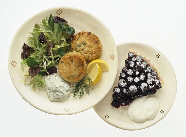 Fish cakes served with salad leaves, herb sauce and sliced lemon and blueberry tart with fresh cream dessert