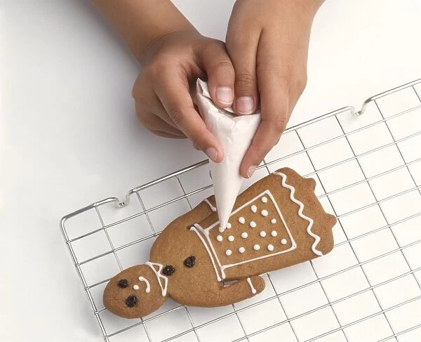 Girls hands piping icing onto gingerbread biscuit on cooling rack, close-up