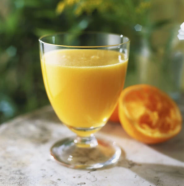 Goblet-shaped glass of orange juice, half of squeezed in background, front view