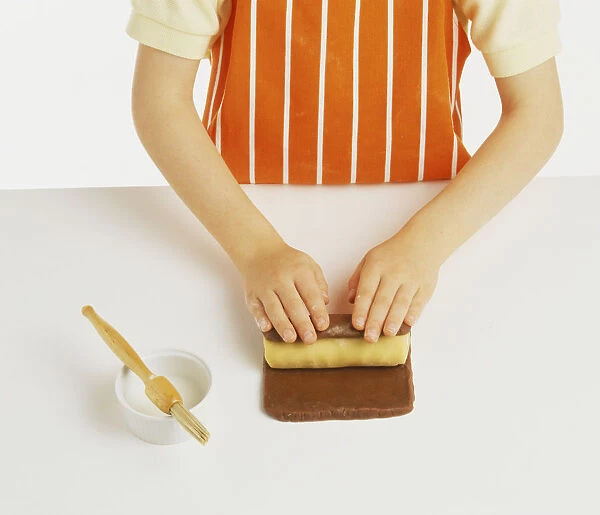 Hand model wearing orange and white striped apron, rolling chocolate shortbread dough around plain