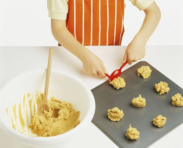 Hand model wearing an orange and white striped apron, spooning peanut butter cookie mixture