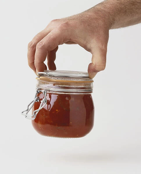 Hand picking up jar of containing heat-processed tomato relish