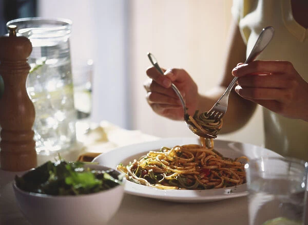 Hands of woman sitting at dinner table twirling spaghetti on a fork using a spoon, side view
